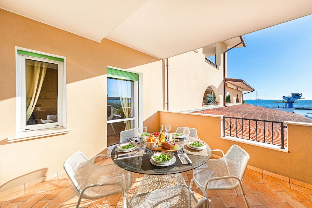 This beautiful three-room apartment directly on the lake with pool and views of Porto Dusano is located in a great holiday accommodation and has Wi-Fi connection!

The air conditioning provides additional comfort throughout the summer. The wide private terrace with lake view and the green surroundings are the perfect combination for your vacation on Lake Garda. The bright living room is a wonderful place to relax; there is a sofa bed for 2 people, a dining table for 6 people, flat screen TV with foreign channels, a modern kitchen with hotplate, refrigerator, freezer, dishwasher, coffee machine, oven, kettle, microwave, citrus press and toaster.

This bright and pet-friendly apartment also impresses with the charming master bedroom, this room has a wardrobe, bedside tables and double bed (a baby bed can be provided here for a small surcharge if required) and the second bedroom with bunk beds. A beautiful bathroom with shower, sink, toilet and bidet completes the furnishings of this carefree retreat.

A private parking space is available to you during your stay for additional comfort.

The pool is available from May 1st to September 30th.