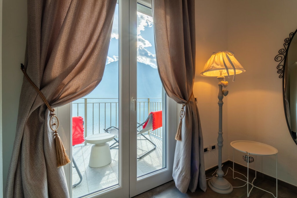 The apartment is located on the ground floor and features an open plan living area with living room, sofa, TV, dining table and a fully equipped kitchen with dishwasher, oven, microwave, kettle, juicer, coffee machine and toaster. The sleeping area has three bedrooms, one with a double bed and two with a French bed each. A bathroom with shower completes the facilities.
The highlight of the apartment is the large terrace equipped with sun loungers from which you can admire the lake and the surrounding mountains.
Guests have at their disposal amenities such as washing machine, iron, free Wi-Fi, air conditioning and heating.
*Guests benefit from an outdoor parking space within the property.