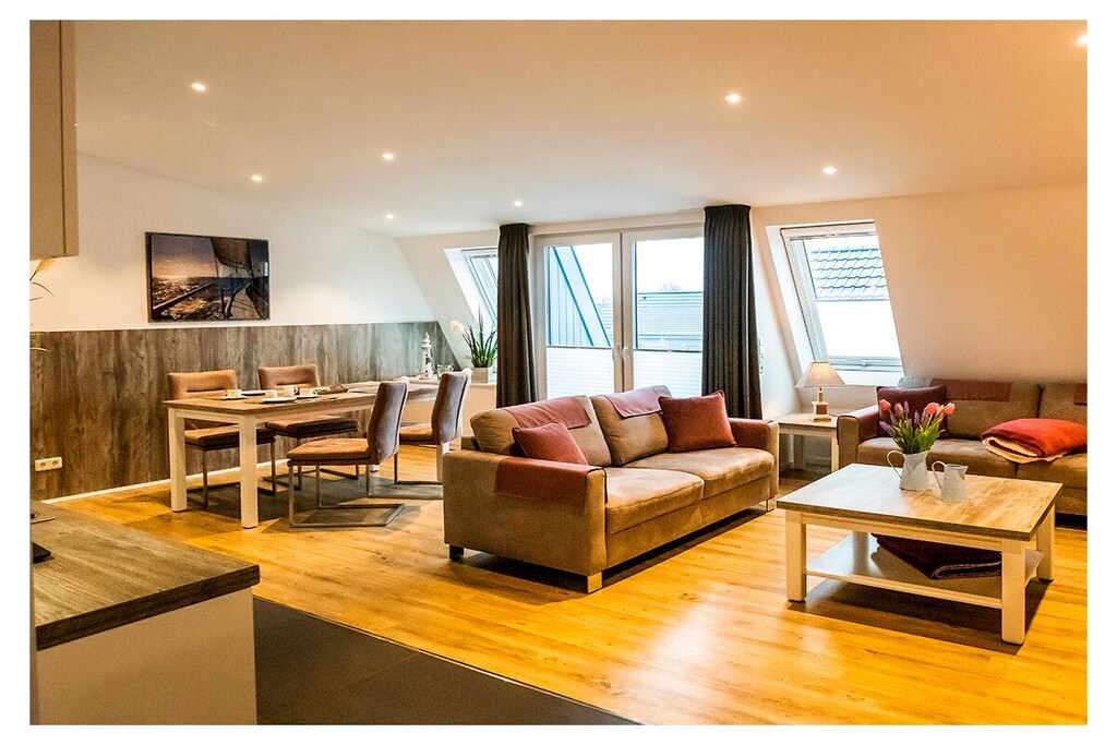 Highlights
This 80 sqm penthouse apartment, completed at the beginning of 2017 and equipped with high quality fittings in Norddeich's prime location, is certainly one of the most beautiful (holiday) apartments on the entire North Sea coast.
The apartment has an exceptionally beautifully designed floor plan. The entire furnishings are deliberately kept at the same high level as the general construction quality (inside and out), this goal was consistently implemented through high-quality local carpentry work such as the built-in cupboards, selected floor coverings, etc.
The apartment is located in the immediate vicinity of the dike, the harbor with the ferry docks to Juist and Norderney, the town center, the beach and the restaurants and offers space for 4 people.
Of course, the entire apartment is equipped with underfloor heating and solar-powered electric window blinds. The very nice and large balcony to this very spacious penthouse rounds off the whole thing.

Apartment facilities
Living room
The new building in Norddeich offers a spacious holiday apartment for 4 people on the top floor. The living, dining and kitchen areas are combined and from there you can also access the balcony. A large TV and a comfortable living area invite you to spend cozy evenings. There is underfloor heating throughout the apartment.
Most of the windows have black-out blinds as well as fly screens and pleated blinds.
You can get a first impression in the 360-degree panoramic view.

Bedroom
In one bedroom there is a double bed (box spring bed) with a large TV. In the other there are 2 single beds. In both bedrooms you can darken the windows, fly screens are available. The little ones sleep in the travel cot that can be delivered. The closet is in the hallway area.
Kitchen
A bright kitchenette with a ceramic hob invites you to cook. Everything that belongs to the kitchen equipment is there: oven, stove, extractor hood