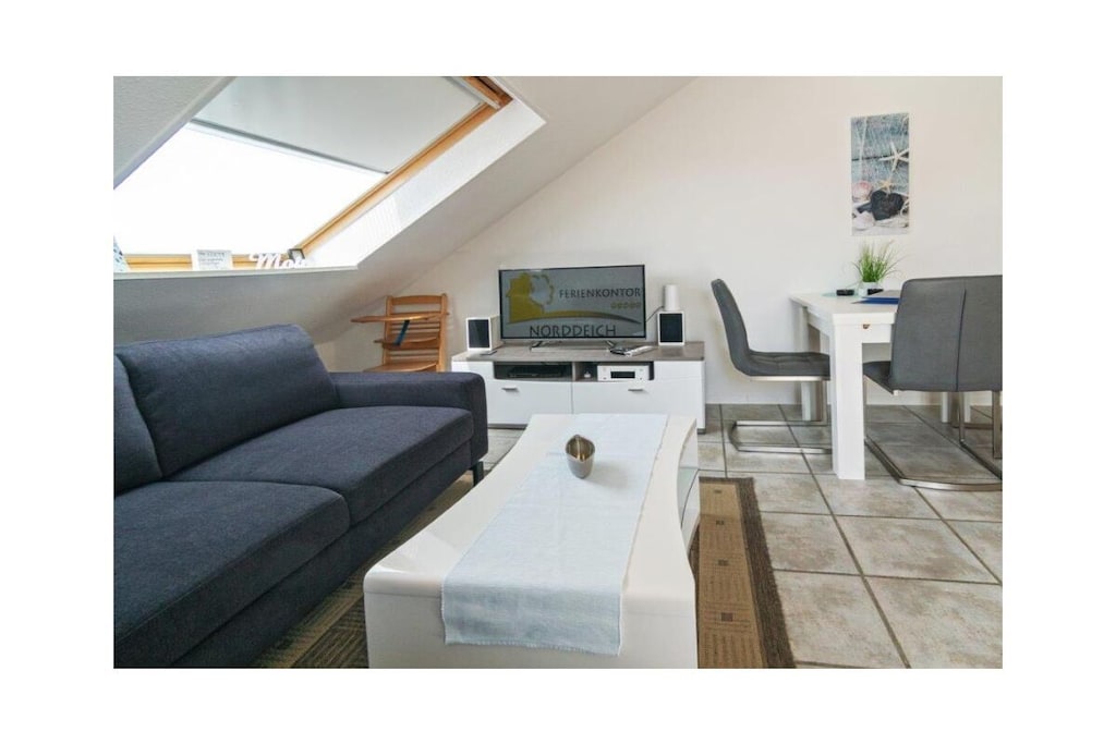 Holiday apartment Nordwind64 - Deichstraße 13, Norddeich, 2nd floor
Pure North Sea feeling - that's what you'll find in Norddeich, a quieter part of the East Frisian town of Norden. The long white sandy beach in particular makes Norddeich a popular holiday resort for North Sea lovers every year. In addition, the lively little center on Dörper Weg with its many small shops and regional culinary offerings is just a few steps away on foot. Norddeich offers you everything your heart desires.
The holiday apartment
Your holiday apartment is located directly behind the dike in a modern apartment complex. This was recently extensively renovated and refurbished, so you can expect a modern design of the highest quality.
Small but nice - this description is more than appropriate for the Nordwind64 holiday apartment. The property is on the 2nd floor and therefore on the top floor of the residential building. A total of 45 square meters of living space exude Nordic coziness and exclusivity at the same time and offer the ideal living comfort for two to three people.
The heart of the apartment is the living-dining area with integrated kitchen. Here you can relax wonderfully on the comfortable living area and spend long evenings watching TV or reading. For media entertainment, you have a modern flat-screen TV with satellite reception, digital TV, a Blu-ray and DVD player, a stereo system and Internet radio. You will also find a selection of DVDs, books and games here, so that you won't get bored even on rainy afternoons.
Cooking together and enjoying a meal in a cozy atmosphere is no problem - thanks to the modern and perfectly equipped kitchenette. Here you have a refrigerator with freezer compartment, oven, ceramic hob with extractor hood, microwave, kettle, (filter) coffee machine, Tassimo coffee machine, toaster, egg cooker, kitchen