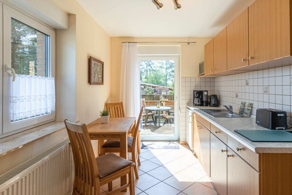 Holiday accommodation at Landhaus Rügeband in Waren (Müritz), a modern one-room apartment (35 sqm) for two adults, featuring a kitchenette, shower/WC, hallway, and terrace with direct garden access. Breakfast room/breakfast service (available upon request), bread roll and beverage service, free bicycle storage, parking space, Wi-Fi, barbecue area, and a park-like garden.