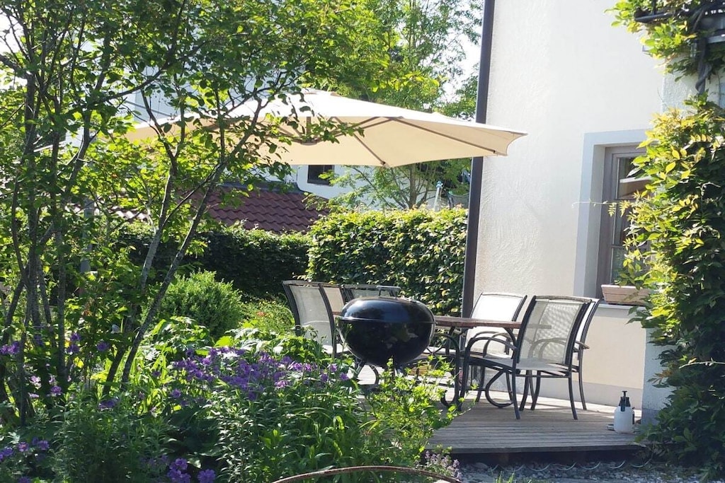 The 48-square-meter holiday apartment is comfortably furnished and offers space for up to four people. It features two separate bedrooms, one bathroom, and a living area with a well-equipped kitchen.
From your south-facing balcony, you have a generous panoramic view of the Alpine foothills and the Alpine chain, stretching from the Salzburg region through the Chiemgau Mountains to the Bavarian Oberland.
Toys and a large playground are also provided for younger guests. A beautiful garden with cozy spots and loungers, as well as a barbecue grill and various places for socializing, await you.
As a special bonus, I offer in-house cosmetic and wellness treatments. I work with the brands "Gertraud Gruber" and "von Lupin."