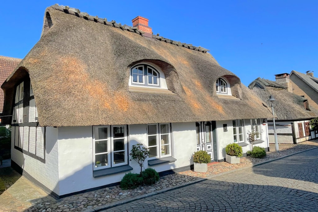 Mentioned in the local chronicle as early as 1806, this house is one of the oldest in the village. It enjoys a quiet location on a small, granite-paved residential street. The banks of the Schlei inlet and the historic boat landings are only about 50 meters away.

We completely renovated the house, taking care to preserve its rustic charm.

The result is a chic, all-white interior with a spacious kitchen, a modern shower room, and a combined living and dining room with a wood-burning stove. The kitchen is fully equipped with a dishwasher, microwave, fully automatic coffee machine, and much more. The bathroom features a Miele washer-dryer. All floors are tiled in shades of gray, making them accessible for people with disabilities.