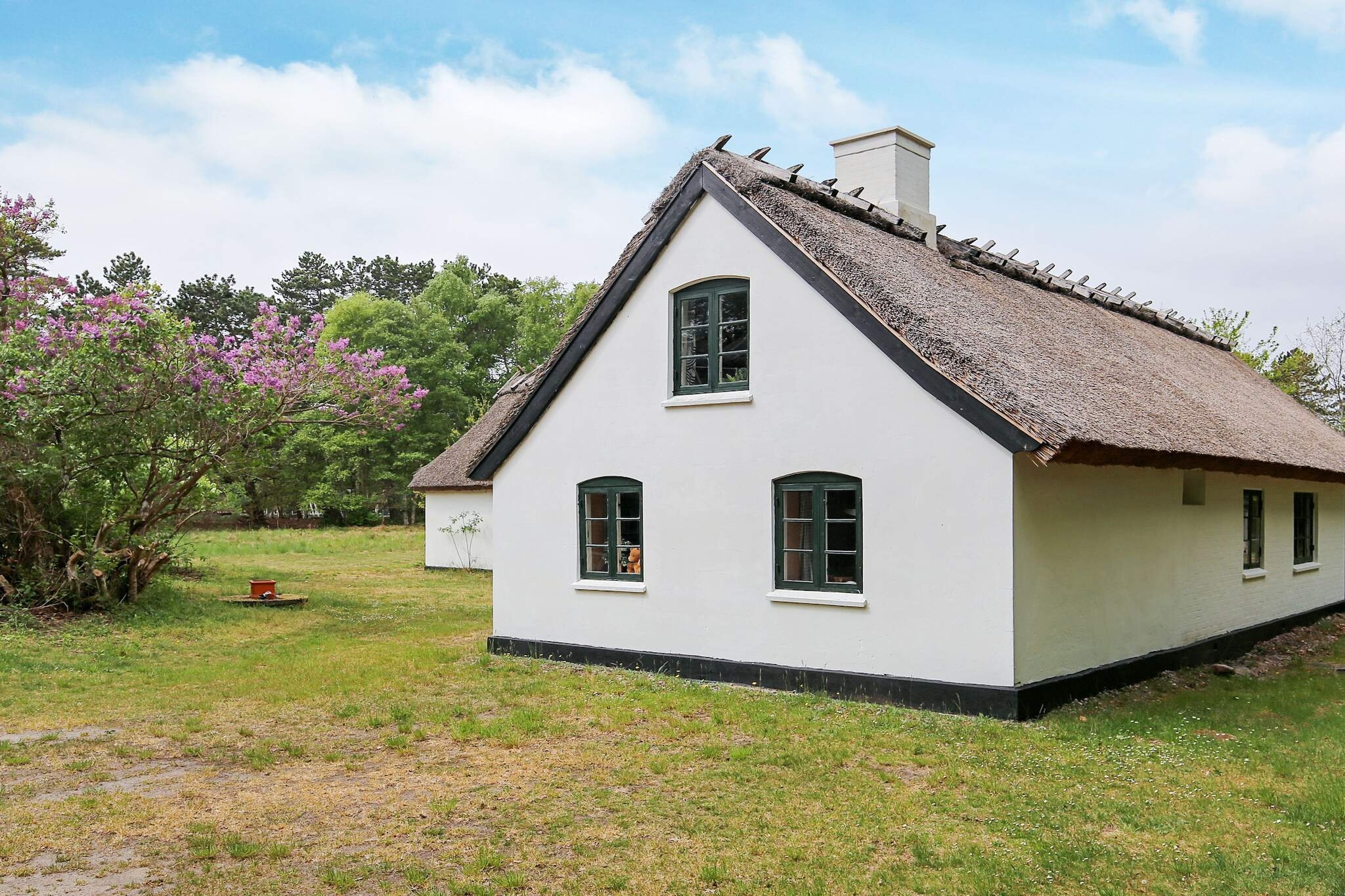 This idyllic thatched holiday home is set on a sprawling 10,000 m² natural plot near Vig Lyng, offering plenty of space for children to play and explore freely. With its authentic character and traditional farmhouse charm, the house is thoughtfully furnished in a style that perfectly matches its rural surroundings, creating a warm and welcoming atmosphere for your stay.
The spacious interior combines comfort with rustic touches. The kitchen is well equipped for family meals, while the dining room with pellet stove invites cozy gatherings. The living room features sloped ceilings, a wood stove, and a fireplace that adds charm to the space, though the fireplace itself is not in use for safety reasons. From here, a staircase leads to a large open loft area (hems) with three extra sleeping places, making it an adventurous retreat for children or additional guests. The ground floor also offers two bedrooms, a bathroom with bathtub, and a second bathroom with shower for convenience. From the entrance hall, a staircase leads to the first floor where you will find a third bedroom, providing a comfortable layout for larger families or groups.
Just a ten-minute walk takes you to the shoreline, along peaceful private paths through the holiday home area. The beach is shallow and child-friendly, ideal for safe play and relaxed seaside moments. On your walk you may even encounter deer in the tranquil surroundings. For the youngest guests, the house is equipped with two high chairs, making it a family-friendly retreat where everyone can feel at home.