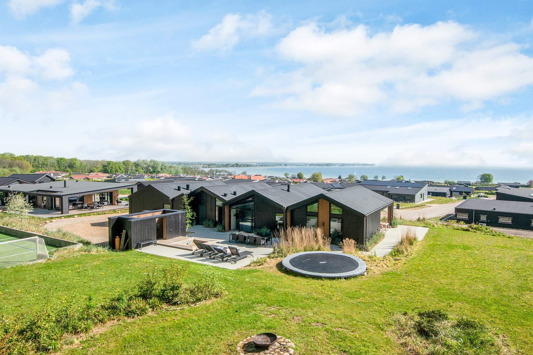 Perched slightly elevated above the beautiful Little Belt, just 500 meters from the shoreline, this modern and climate-friendly holiday home offers the perfect setting for a memorable getaway. Designed for up to 12 guests, the house combines contemporary comfort with thoughtful details, all surrounded by serene natural beauty. With the peaceful forest as its closest neighbor and wide panoramic views of the water, it is a retreat that brings you close to both nature and relaxation.
At the heart of the house lies the spacious open-plan living and dining area, seamlessly connected to a well-equipped kitchen. Here, large windows invite daylight to flood the room, creating an airy and welcoming atmosphere. Enjoy your morning coffee as the sun rises over the Little Belt, while the forest behind the house frames the scene with its calming greenery.
The highlight of the property is undoubtedly its 24 m² swimming pool, perfect for fun and relaxation at any time of year. For those seeking even more indulgence, the adjoining whirlpool provides a soothing space to unwind after a day of exploring. Two modern bathrooms and a practical utility room with washer and dryer make the home equally functional for longer stays.
Accommodation is spread across four comfortable bedrooms, each furnished with double beds for a restful night’s sleep. For larger groups or families, two additional sleeping lofts upstairs each provide two extra places, especially popular with children who love their own cozy hideaway.
Step outside from the living room onto the expansive terrace, where a gas grill awaits for summer barbecues. Here, you can gather with family and friends, dine under the open sky, and enjoy uninterrupted views of the water. Whether you’re swimming in the pool, relaxing in the whirlpool, or simply savoring the natural surroundings, this home promises unforgettable moments.
Please note: rentals are not permitted for youth or tradesmen groups.