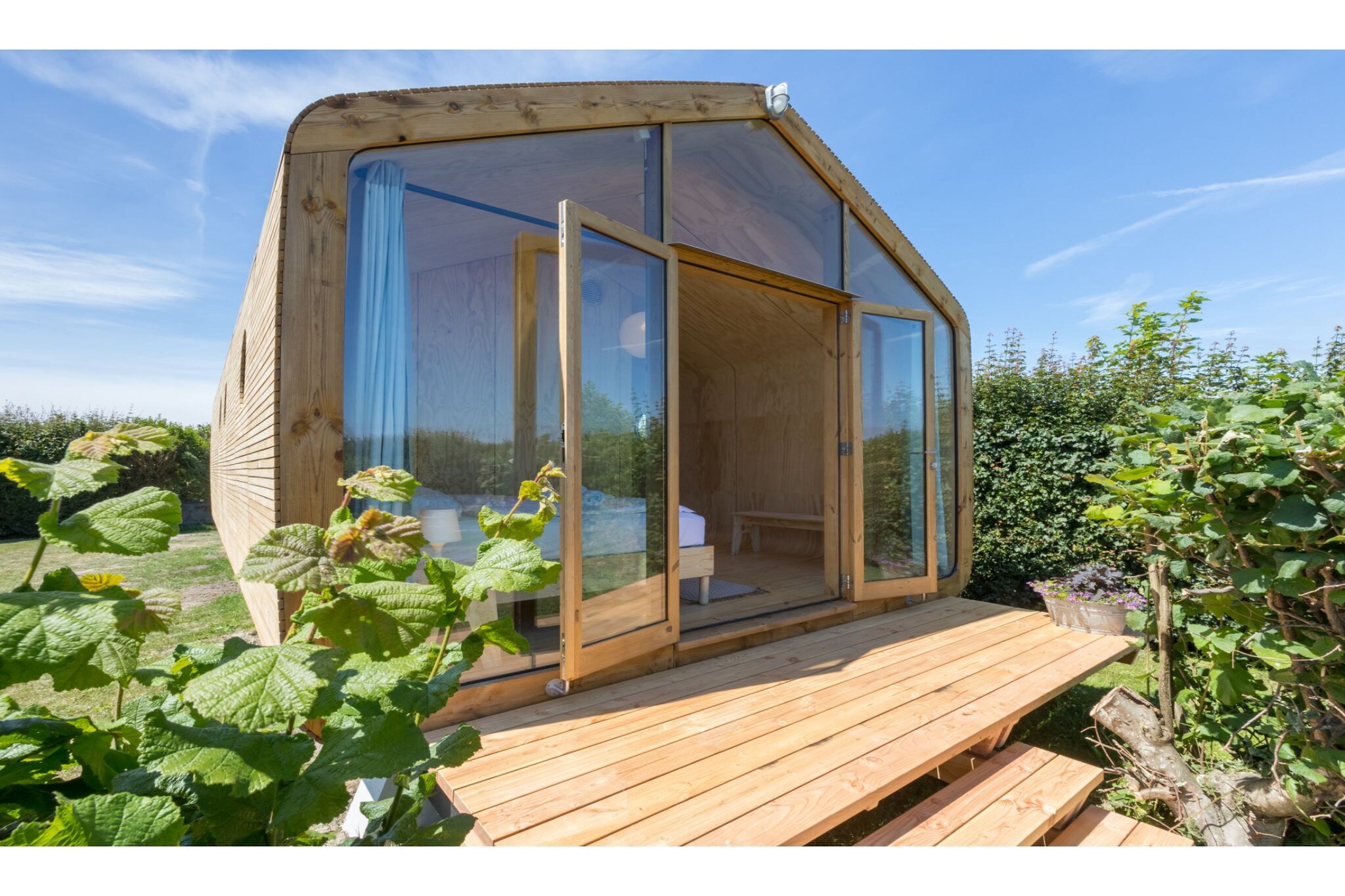 Welcome to this unique wrapping house, built from sustainable materials such as wood, cardboard, and flax. Located on a relaxed arable farm in Zeeland, it offers plenty of space to unwind, while children can enjoy the trampolines, swing, slide, go-karts, and sandbox. Take a long morning walk through the dunes of Oranjezon or watch the sunset from your garden — moments you’ll remember forever.
The tiny house is on the ground floor and reached via a staircase with three steps. Glass panels at the front and rear allow plenty of natural light inside. Rounded corners and a wooden, quiet interior create a cozy atmosphere that makes you feel immediately at home. The house is equipped with air conditioning, and a washing machine is available for general use (for a fee).
At the front, you enter the kitchen, which includes a dishwasher, fridge with freezer compartment, kettle, and Nespresso machine. The bathroom, located in the middle of the house, has a shower, sink, mirror cabinet, and toilet. The two bedrooms are situated at the rear and center of the house, making it convenient for children who go to bed early. Both bedrooms have a box spring (160x200 cm) and two bedside tables. A high chair and folding baby bed (60x120 cm) are also available.
De Specht has its own terrace at the front and rear (25 m² in total), and a large garden surrounds the house, screened with plants (no fence). There is plenty of space to play, and you can enjoy beautiful views of the dunes and farmland. Barbecues are allowed except during dry periods due to fire risk.
Bicycles can be stored inside the bicycle shed, located on the other side of the sanitary building of the adjacent mini-camping.