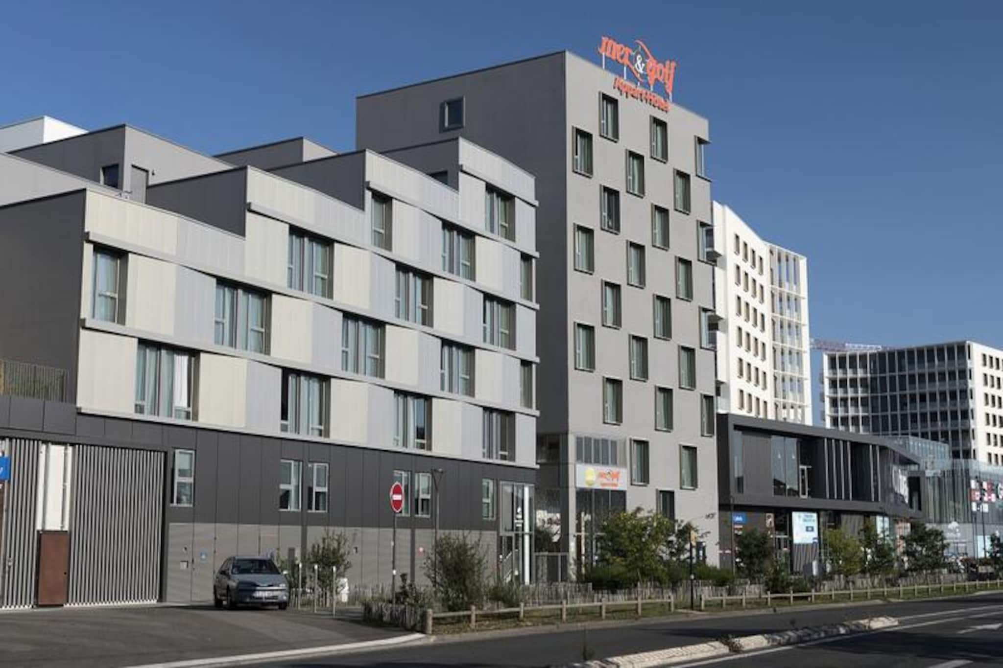 This modern and well-located apartment hotel is situated in the heart of the Bordeaux Ginko eco-district, making it the ideal base for both business and leisure travelers. Positioned near the Parc des Expositions, Palais des Congrès, Stade Matmut Atlantique, and Lac de Bordeaux, guests can enjoy easy access to these key attractions. The surrounding area is a mix of urban and natural spaces, with pedestrian alleys, shopping options, communal gardens, and scenic canals enhancing the environment.

The residence boasts 97 spacious and bright apartments, ranging from studio to larger units, all air-conditioned and designed for comfort. Most apartments feature south-east or north-west facing views, ensuring plenty of natural light. Guests can enjoy amenities like a fitness room, laundry facilities, and a breakfast area with a terrace overlooking a tranquil patio filled with trees.

Located just 100 meters from the tram line C, guests can easily travel to the city center or the train station. For those looking for more leisure activities, the Calicéo aquatic fitness center, covering over 4000m², and the nearby lake beach offer great relaxation options. Additionally, the residence is close to various shops and restaurants, with a lively atmosphere combining convenience and calm.

Whether visiting for a conference, a game at the stadium, or a relaxing holiday by the lake, this apartment hotel provides a perfect balance of comfort, location, and amenities.