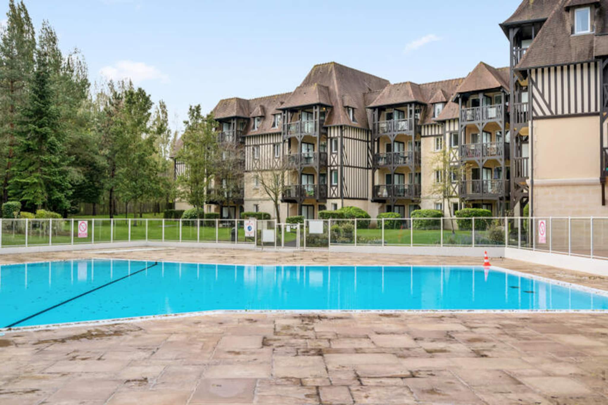 Nestled in a serene, green environment, this cozy apartment features a blend of traditional Norman architecture and modern comforts. Perfect for up to four guests, it offers a comfortable bedroom with a double bed and a living room with a sofa bed for two. A south-facing balcony provides stunning views of the golf course, while outdoor parking ensures convenience. Pets are welcome, making this a great choice for families and couples alike.

Located on the heights of Deauville, the apartment is just 2.5 km from the iconic “Planches” boardwalk and around 2 km from the Thalasso Deauville spa. Spend your evenings at the renowned Casino Barrière or attend thrilling horse races at the nearby Deauville-La Touques Hippodrome. With golf, tennis, and equestrian centers all within 500 meters, it’s an ideal spot for active travelers.

The apartment features a fully equipped American-style kitchen with modern appliances and a dining area for four. The bathroom includes a bathtub, towel dryer, and storage space, while additional amenities like a heated outdoor pool (open seasonally) and optional Wi-Fi ensure a comfortable stay. End-of-stay cleaning services are mandatory, ensuring a hassle-free experience.