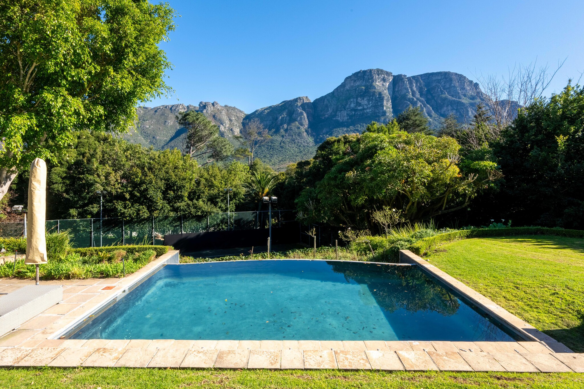 Elegant Family Retreat in Prestigious Bishopscourt, Cape Town

Welcome to your serene escape in the heart of Bishopscourt, one of Cape Town’s most exclusive and picturesque suburbs, nestled beneath the majestic Table Mountain range. This spacious and elegant home offers four generous en-suite bedrooms, thoughtfully designed for both comfort and privacy. The open-plan living and dining area flows seamlessly into a modern kitchen, creating a warm and inviting space for relaxed holiday living.

A dedicated entertainment and games room provides fun for all ages, while the outdoor setting is nothing short of spectacular. Rolling green lawns stretch out to a sparkling swimming pool and a private tennis court, all framed by breath taking mountain views.

Bishopscourt is known for its tranquil, leafy surroundings and proximity to some of the city's best-loved attractions. From here, you’re just a short drive from Kirstenbosch Botanical Gardens, Constantia’s award-winning wine estates, and the pristine beaches of the Atlantic Seaboard.

Whether you're looking to unwind in peaceful luxury or explore the vibrant city, this exceptional home offers the perfect base for your Cape Town stay.