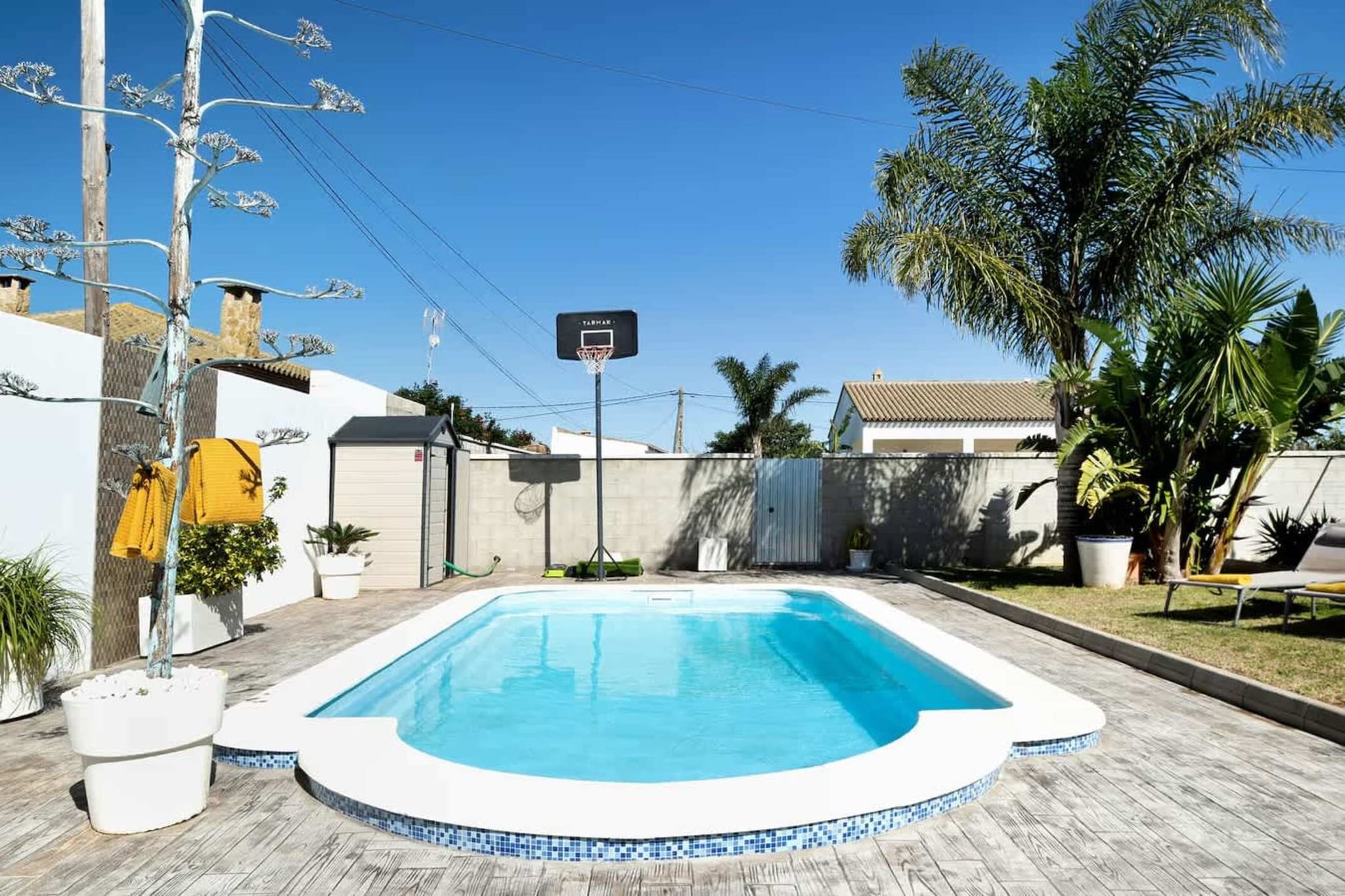 Some places are made for resting, others for playing, this villa gives you both. Imagine cooling off with a dip in the pool and then taking your shot at the basketball hoop set just beside the water. Whether it’s splashing contests with the kids, lazy afternoons in a hammock, or friendly games that last past sunset, every corner of this home is built for joy. 

The villa sits within a private fenced plot, so peace and privacy are guaranteed. The garden is spacious and inviting, with a porch perfect for outdoor dining, sun loungers for lazy siestas, and a solar shower for freshening up after a swim. Inside, the design is modern yet warm: a living room for movie nights, a kitchen equipped with everything from oven to dishwasher, and three bedrooms that promise comfort at the end of each day. The master bedroom even comes with its own ensuite and walk-in closet, a little luxury for your holiday routine. What makes this spot truly special is how it blends homey comfort with playful touches. It’s a place where families can spread out, friends can share laughter, and couples can find their own private nook.

Nearby, just 10 minutes away, the beaches of Los Bateles and La Fontanilla invite you to sink your toes in golden sand and watch the horizon glow at dusk. Conil’s Old Town, with its tapas terraces and whitewashed streets, is perfect for evening strolls. Golfers can head to Club de Golf Campano (12 km), while nature lovers will love the trails of La Breña Natural Park and the sweeping views from Cape Trafalgar.