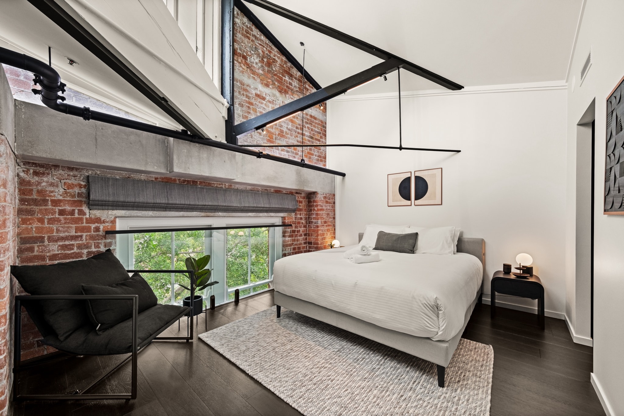 Property description
Located in an iconic Woolstore building along the riverfront, this stylish two-bedroom apartment blends historic charm with modern comforts. Enjoy spacious living areas, a well-equipped kitchen, and ducted A/C throughout. The master bedroom features an en-suite, while both bathrooms offer sleek, modern fittings. Relax by the riverside pool or take a stroll along the scenic Riverwalk. Offers private laundry, onsite parking, and easy access to cafes and transport, making it an ideal urban retreat.
The space
Blending industrial charm with contemporary elegance, this two-bedroom apartment captures the character of Teneriffe’s iconic Woolstores. Exposed brick walls and warm timber floors create a striking backdrop for the inviting living space, complete with a large three-seater couch and natural décor. The king and queen bedrooms are bright and restful, with blackout blinds for privacy and restful sleep. Two sleek bathrooms, one an en-suite, feature modern fittings. The open kitchen includes an induction stovetop and electric oven, adjoining a dining area that seats four, plus four countertop stools for casual meals. Upstairs, a private laundry adds convenience, while ducted air conditioning ensures comfort throughout. With access to a riverside pool and direct entry via stairs, this unique apartment is perfect for travellers seeking an architectural gem in a lively neighbourhood.