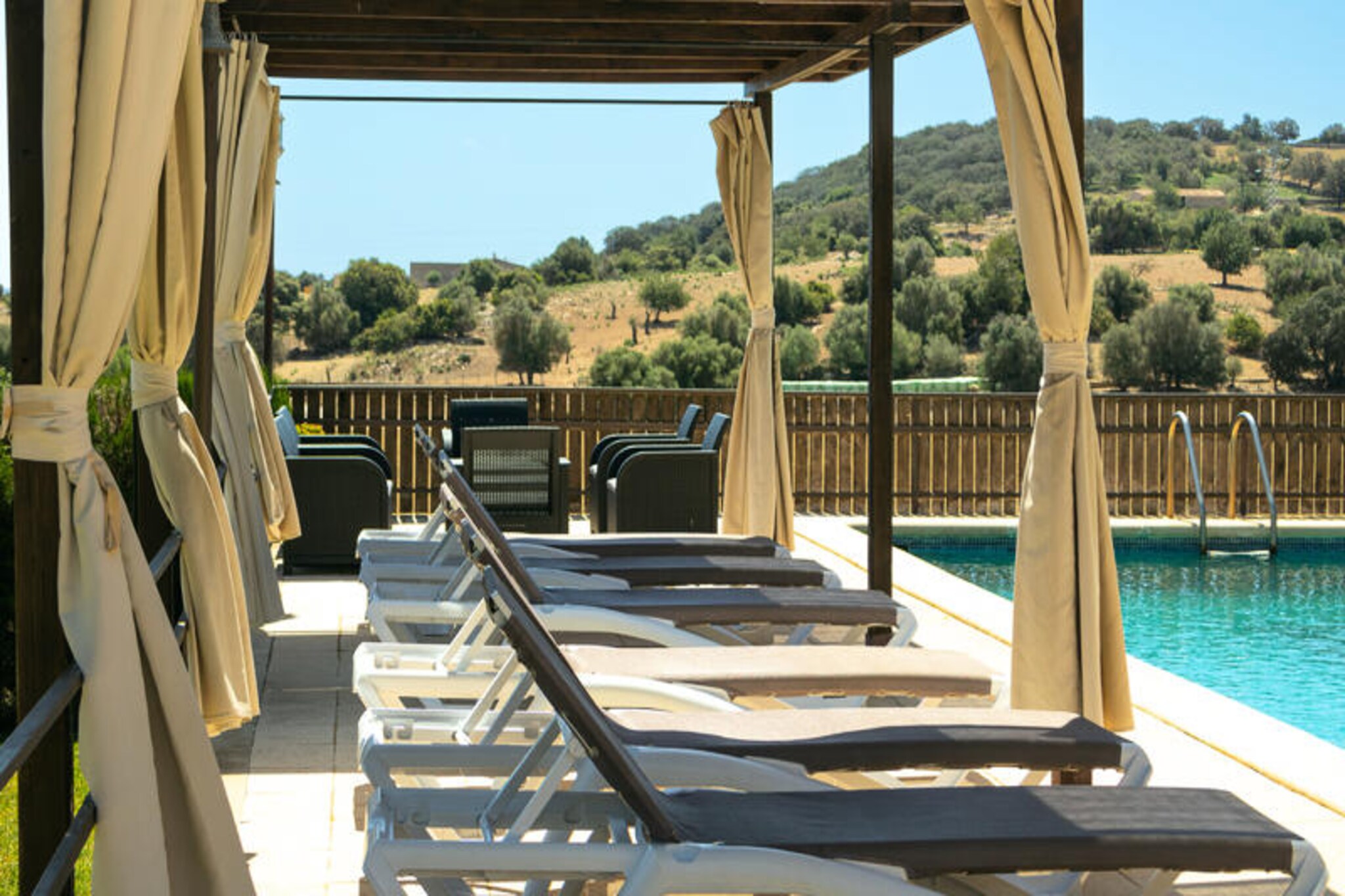 Amidst the serene landscapes of Llubí, this exquisite villa offers a tranquil escape for families and groups seeking a blend of relaxation and adventure. Surrounded by lush greenery, the property is a haven of peace, where the gentle rustle of leaves and the chirping of birds set the tone for your stay. With its expansive grounds and thoughtful amenities, this retreat promises unforgettable moments under the Mallorcan sun.
The villa boasts six spacious double bedrooms, each with its own en-suite bathroom, ensuring privacy and comfort for all guests. One of the bathrooms is thoughtfully designed for guests with reduced mobility, featuring an extra-wide door and a small ramp. The open-plan living area, complete with a fully equipped kitchen and a large dining table, is perfect for family gatherings. Step outside to discover a 250 m² terrace, ideal for al fresco dining, complete with a barbecue for preparing delicious meals over a wood fire. The large swimming pool, surrounded by sun loungers, invites you to unwind, while the private tennis court and children’s playground offer entertainment for all ages.
Located less than 10 km from some of Mallorca’s most stunning beaches, the villa is perfectly situated for days spent by the sea. Explore the nearby hiking and cycling trails, or immerse yourself in the charm of Llubí, a traditional Mallorcan village known for its welcoming atmosphere and cultural heritage. Don’t miss the chance to savor local gastronomy at nearby restaurants or visit the historical sites that dot the region.
Whether you’re lounging by the pool, enjoying a game of tennis, or exploring the natural beauty of Mallorca, this villa provides the perfect backdrop for cherished memories. Experience the authentic essence of the island in this idyllic retreat, where every detail is designed to make your stay extraordinary.