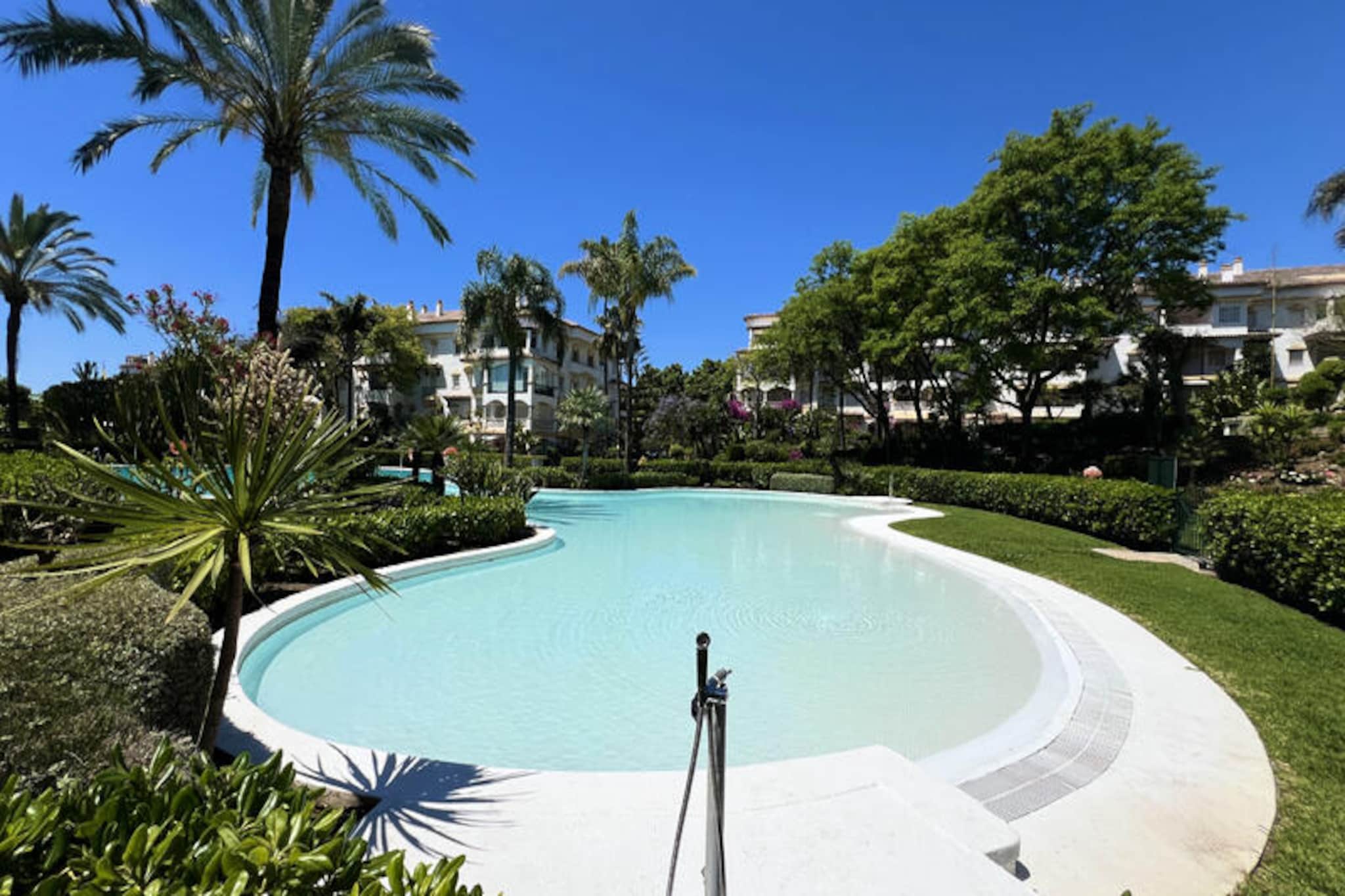 In the heart of Nagüeles, just moments from the vibrant Puente Romano neighborhood, this spacious apartment offers a serene retreat amidst the lively charm of Marbella. Imagine starting your day with a stroll to chic cafes and restaurants, or a short walk to the beach where the promenade connects Marbella center to the glamorous Puerto Banús. The apartment’s shaded terrace invites you to unwind with a refreshing drink, surrounded by the gentle hum of tropical gardens and the soothing sound of waterfalls. \n\nInside, the apartment boasts a modern, open-plan living space with an American-style kitchen, perfect for preparing meals after a day of exploring. Three simply decorated bedrooms and two bathrooms provide ample space for families or groups of friends. The development itself is a haven of relaxation, featuring a large swimming pool, paddle tennis courts, and lush gardens teeming with green parakeets and exotic flora, evoking the feel of a Costa Rican jungle.\n\nWith its prime location just 100 meters from local shops and restaurants and 400 meters from the beach, everything you need is within easy reach. Whether you're soaking up the sun by the pool, enjoying the vibrant nightlife of Puente Romano, or exploring Marbella's historic old town, this apartment is the perfect base for your Costa del Sol adventure. \n\nBook your stay today and experience the perfect blend of relaxation and excitement in one of Spain's most sought-after destinations.