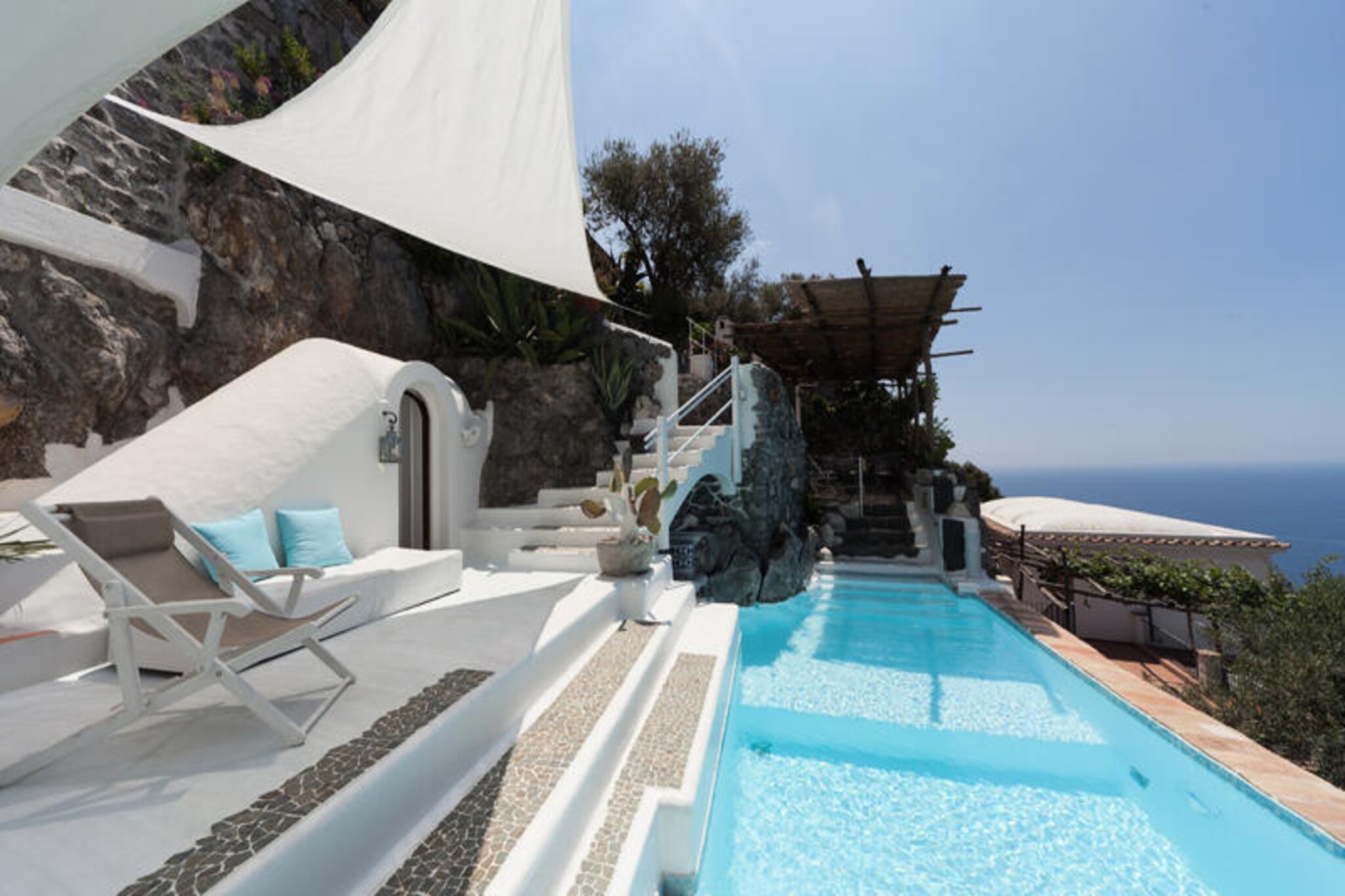 Perched above the sparkling Tyrrhenian Sea, Villa Venusta is a masterpiece of elegance and tranquility, offering an unforgettable escape in the heart of Praiano. This luxurious villa, crafted from whitewashed limestone and adorned with intricate wrought iron and stone details, embodies the charm of Arabic architecture. Surrounded by fragrant lemon groves and olive trees, the villa boasts panoramic views of Capri, the Li Galli islands, and the vibrant sunsets that paint the sky over Positano in hues of orange and pink. Here, serenity meets sophistication, far from the bustling summer crowds. \n\nInside, the villa is a harmonious blend of history and modern comfort. With four exquisitely furnished bedrooms featuring vaulted ceilings, ancient capitals, and period furniture, every corner tells a story of timeless beauty. The villa spans three levels, offering a spacious dining room with handmade terracotta tiles, a fully equipped kitchen with industrial-grade appliances, and a sea-view living room. Guests can indulge in ultimate relaxation with a private massage room, a wooden sauna, and a panoramic outdoor pool with a whirlpool area. The villa also features a private wine cellar with over 100 premium Italian and French labels, perfect for wine enthusiasts.\n\nVilla Venusta’s location is both convenient and peaceful. Free parking for two vehicles and step-free access make it easily accessible. Within walking distance, you’ll find local and SITA bus stops, grocery stores, and charming restaurants. For beach lovers, the Fire Beach Club is just moments away. Whether you’re exploring the Amalfi Coast or enjoying the villa’s luxurious amenities, every moment here feels like a dream.\n\nChoose Villa Venusta for an unparalleled experience of Italian elegance, breathtaking views, and the perfect blend of relaxation and adventure. Let the sunsets over Capri and Positano become the backdrop to your most cherished memories.