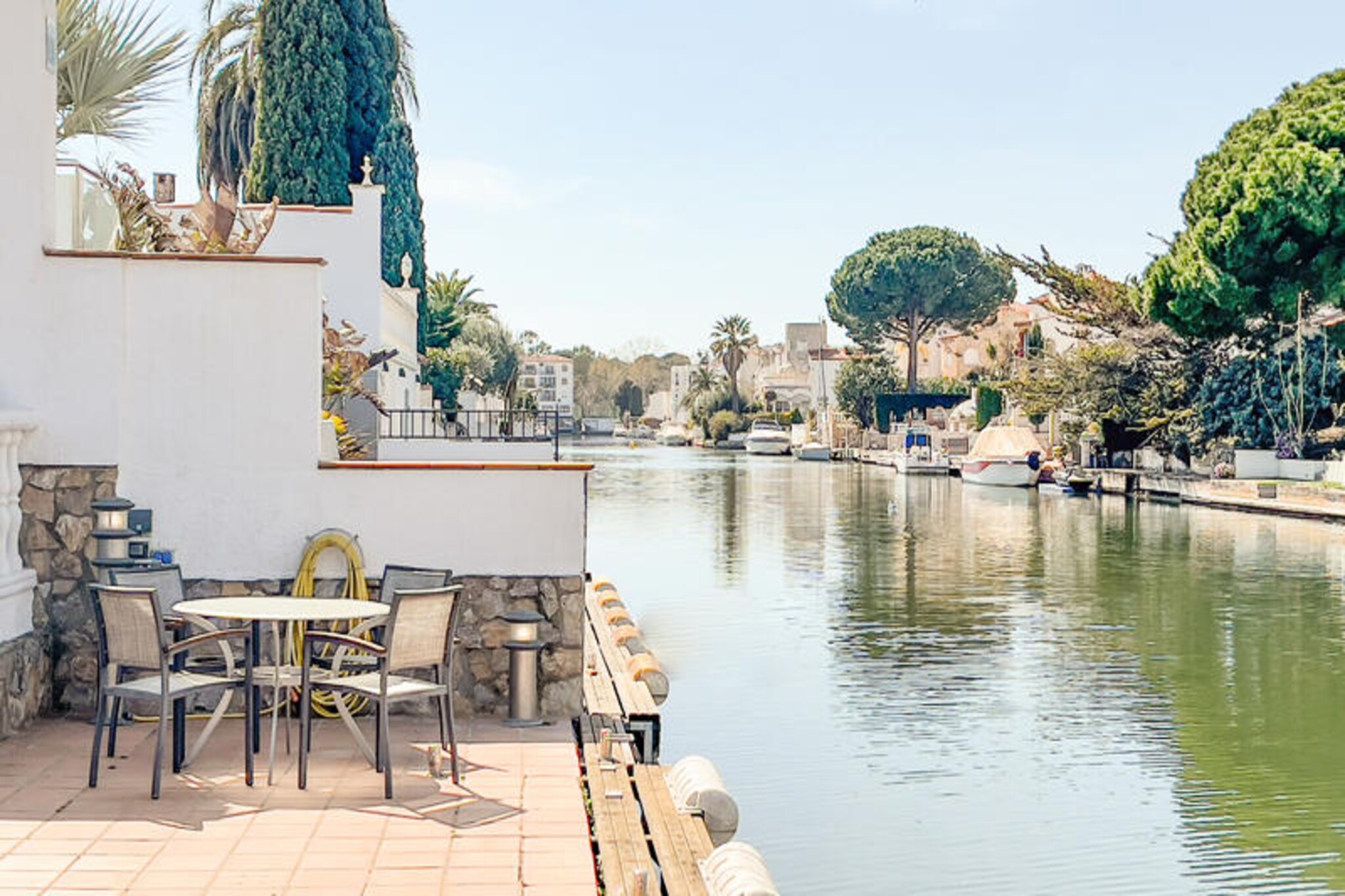 Imagine waking up to the gentle sound of water lapping against the dock, as the morning sun filters through the lush greenery of your private garden. Villa Canals in Empuriabrava offers a serene retreat for families and friends seeking a luxurious getaway on the Costa Brava. With its unique location along the canals, this villa provides direct water access, perfect for boating enthusiasts or those simply looking to unwind by the pool in a tranquil setting. \n\nStep inside and be transported to a world of retro elegance with the villa’s 70s-inspired design. The spacious interior is thoughtfully equipped with modern amenities to ensure your comfort. A fully equipped kitchen and a large dining table for up to 10 guests make it easy to enjoy meals together, while the cozy living room with a fireplace invites you to relax after a day of exploring. The villa accommodates up to 7 guests across three comfortable bedrooms, including a master suite with an en-suite bathroom featuring a massage bathtub. \n\nOutside, the villa truly shines. The expansive garden, complete with a private pool and a fully fenced area, offers ample space for relaxation and outdoor dining. The outdoor kitchen with a grill and covered seating area is perfect for al fresco meals, while the private dock allows you to explore the canals at your leisure. \n\nLocated just minutes from the vibrant center of Empuriabrava, you’ll find charming shops, restaurants, and historical landmarks like Castelló d'Empúries nearby. For thrill-seekers, the town is a renowned skydiving destination, offering breathtaking views of the coastline. Whether you’re here to relax, explore, or seek adventure, Villa Canals is your gateway to an unforgettable Costa Brava experience.