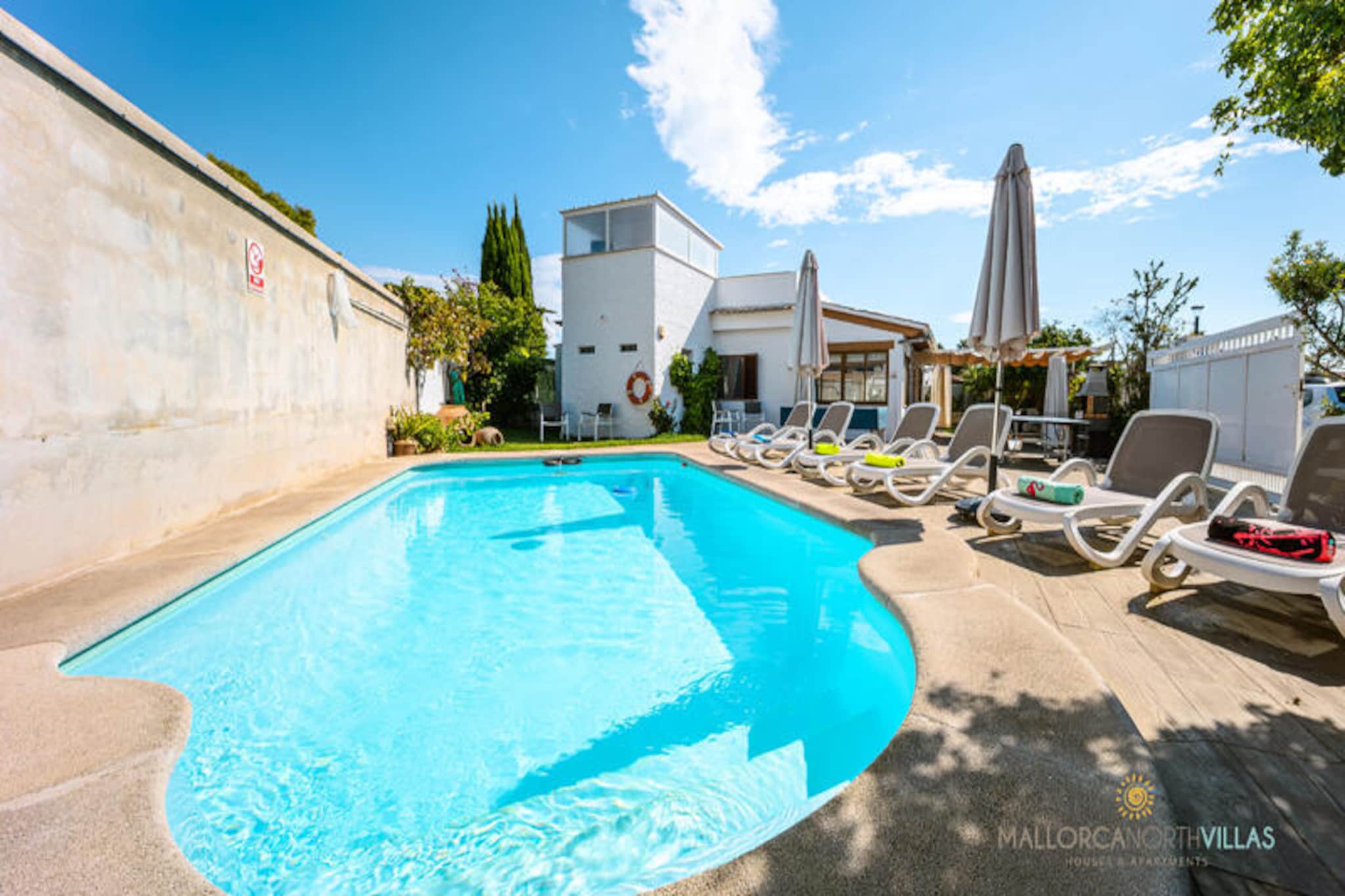 Bathed in the golden glow of Mallorca’s sun, Villa Luna offers a serene retreat just 700 meters from the sandy shores of Puerto de Alcúdia. This inviting villa is a haven for families or groups of friends seeking both relaxation and adventure on the island. Imagine waking up to the gentle Mediterranean breeze, stepping onto the terrace, and planning a day filled with beachside fun or exploring the nearby historic gems of Alcúdia. \n\nThe villa boasts a private outdoor swimming pool surrounded by lush greenery, perfect for refreshing dips under the Mallorcan sky. The spacious terrace features a barbecue and a covered dining area, ideal for enjoying al fresco meals with loved ones. A ping-pong table and cozy garden furniture add to the outdoor charm, while the lighting ensures evenings are just as magical as the days. Inside, the bright and airy living and dining room is flooded with natural light from large windows, creating a welcoming space to unwind. The fully equipped kitchen includes modern conveniences such as a gas stove, refrigerator, microwave, and even a drinking water filtration system for added comfort. \n\nVilla Luna accommodates up to six guests across three bedrooms, including one double room and two twin rooms, two of which feature en-suite bathrooms. All rooms are equipped with air conditioning and heating, ensuring a comfortable stay year-round. The villa’s energy-efficient schedule reflects a thoughtful approach to sustainability. \n\nLocated near Bellevue and Ciudad Blanca, guests can easily access a variety of restaurants, shops, and leisure activities. The historic center of Alcúdia, with its charming market held on Tuesdays, is just a short drive away. For nature enthusiasts, the nearby Puig de Sant Martí offers scenic hiking trails and breathtaking views. Whether you’re seeking tranquility by the pool or adventures in the vibrant surroundings, Villa Luna promises an unforgettable Mallorcan escape.