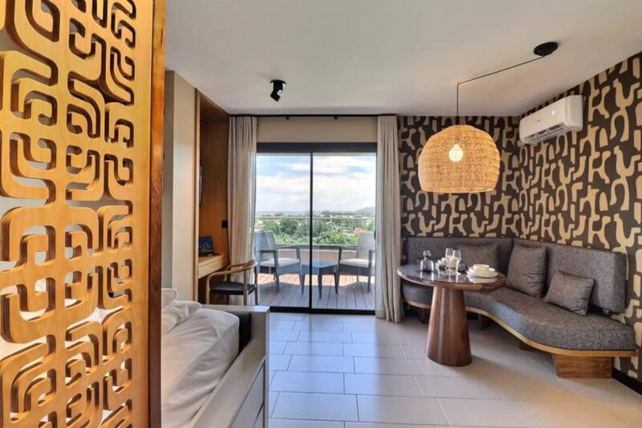 High above the vibrant streets of Papeete, the Mahana Suite offers a breathtaking escape where cityscapes meet the turquoise lagoon and lush mountains. Situated on the 8th floor of the newly renovated Lagon Bleu residence, this modern retreat invites you to immerse yourself in the beauty of Polynesia while enjoying the comforts of contemporary living. From the panoramic terrace, watch the sun rise over the ocean or the city lights sparkle against the night sky—a view that feels like a living postcard every moment of your stay.\n\nStep inside and discover a space designed for relaxation and elegance. The suite is fully air-conditioned, ensuring comfort in the tropical climate, and features a refined décor with meticulous finishes. The light-filled living room opens onto the terrace, creating a seamless connection between indoor and outdoor living. A cozy sleeping area, separated by an elegant decorative partition, offers privacy, while the modern kitchen is equipped with everything you need, including a stovetop, coffee maker, and washing machine. High-speed Wi-Fi and a smart TV provide entertainment and convenience, making this suite ideal for both leisure and business travelers.\n\nGuests of the Mahana Suite also enjoy exclusive access to the amenities of the Lagon Bleu residence. Cool off in the swimming pool under the Tahitian sun or energize in the well-equipped gym. Whether you’re here to explore the wonders of Polynesia or simply unwind, this residence provides the perfect balance of urban sophistication and island charm.\n\nWith its unbeatable location, stunning views, and luxurious amenities, the Mahana Suite is your gateway to experiencing the magic of Papeete in style and comfort.