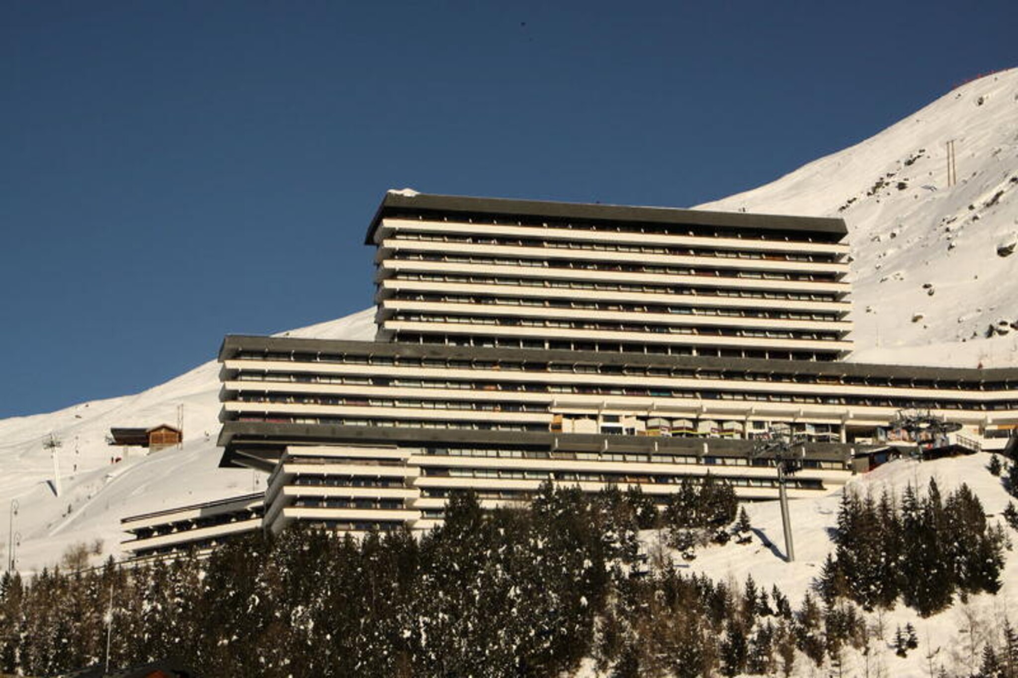 High above the charming Les Menuires resort, the Brelin building offers a unique vantage point with breathtaking views of the surrounding alpine landscape. Perched just above the lively La Croisette district, this cozy duplex studio apartment provides a peaceful retreat while remaining conveniently connected via 24/7 public elevators. Here, you can wake up to the warmth of the sun streaming through your south-facing balcony and enjoy the serenity of the mountains. \n\nThis 24 m² studio is thoughtfully designed to accommodate up to four guests, making it ideal for couples or small families. The living area features a fold-down double bed and a comfortable sofa, complemented by a television for cozy evenings in. A sleeping alcove under the stairs offers two single bunk beds, perfect for children or additional guests. The apartment is equipped with a modern kitchen, including ceramic hobs, an oven, a microwave, a dishwasher, and all the essentials for preparing hearty meals after a day on the slopes. The bathroom features a shower, and there is a separate WC for added convenience. \n\nThe Brelin building itself is home to a shopping arcade with ski lift ticket offices and essential shops, ensuring everything you need is just steps away. Ski lockers on the ground floor provide easy storage for your gear, while free parking at the Evons lift makes arrival and departure hassle-free. With its prime location, you’ll have direct access to the slopes and the vibrant energy of Les Menuires. \n\nWhether you’re here to ski, hike, or simply relax in the crisp mountain air, this apartment offers the perfect base for your alpine adventure. With its stunning views, convenient amenities, and cozy atmosphere, it’s a place where unforgettable memories are made.