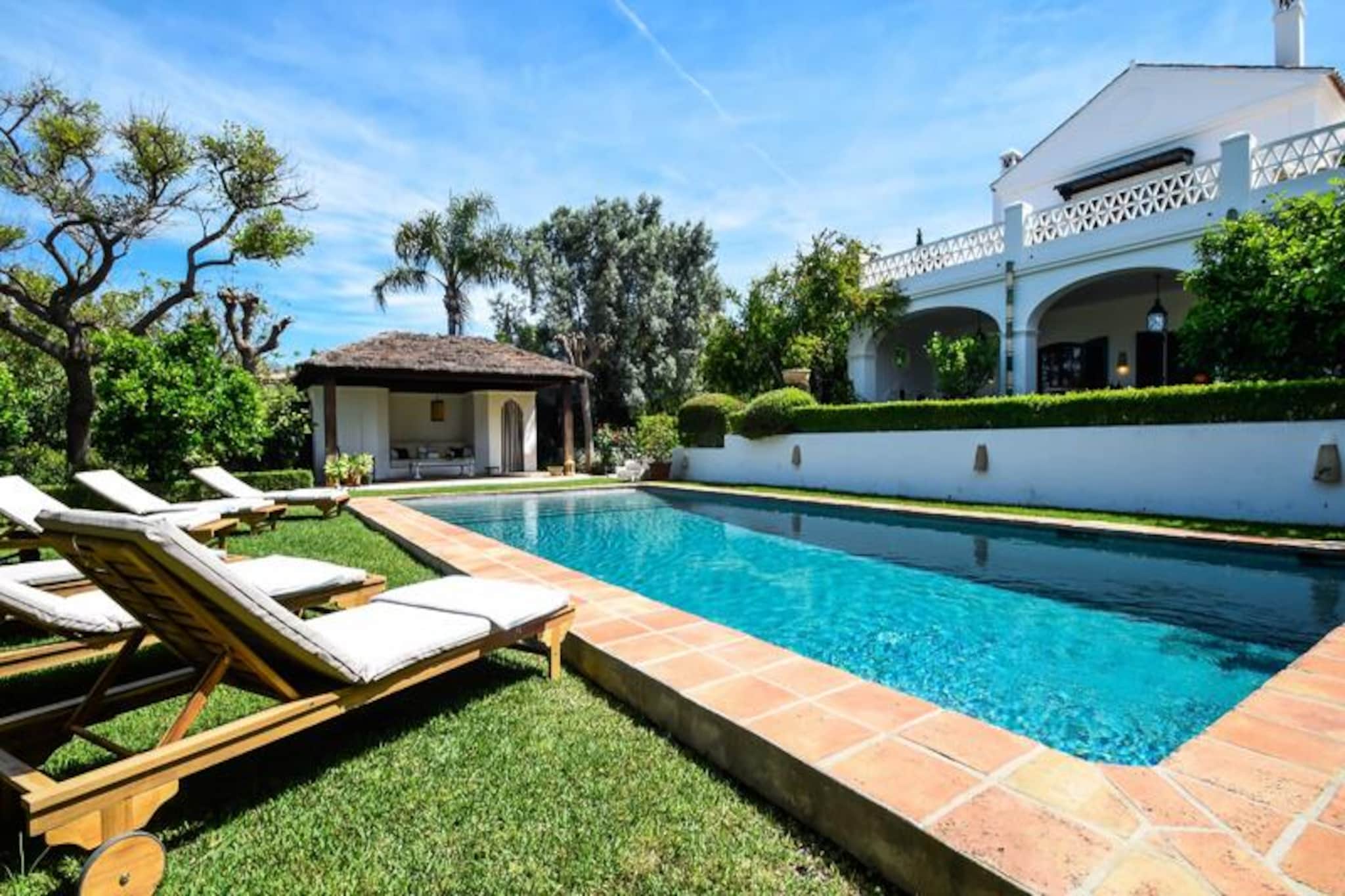 Amid the serene charm of Andalusia, this exquisite colonial-style villa offers an idyllic retreat just moments from the golden sands of the Mediterranean. With its elegant architecture, lush gardens, and a private heated swimming pool, this property is the epitome of relaxation and sophistication. Whether you're soaking up the sun by the pool or enjoying the gentle sea breeze on the terrace, every moment here feels like a dream come true.
Step inside and be greeted by the villa's timeless elegance. The antique wooden door opens to high ceilings and a spacious hallway that leads to a beautifully designed living area, a fully equipped kitchen with a cozy breakfast nook, and six luxurious bedrooms. Four of the bedrooms feature en-suite bathrooms, ensuring comfort and privacy for all guests. The master suite on the first floor boasts direct access to a private terrace with breathtaking views of the Mediterranean, perfect for unwinding with a book or a glass of wine.
The outdoor spaces are equally enchanting. A large covered terrace with a dining area for 12, a barbecue, and a comfortable lounge invites you to enjoy long, leisurely evenings under the stars. The southwest-facing garden, with its vibrant greenery and poolside sun loungers, is a haven of tranquility. The pool house, complete with a sofa, offers a shaded retreat on sunny afternoons.
Located in a quiet residential area, the villa is just a short stroll from the beach, where you'll find charming chiringuitos, beach clubs, and restaurants. For those seeking adventure, the vibrant old town of Marbella is only 6 km away, while the glamorous Puerto Banús marina, with its luxury boutiques and nightlife, is a 15-minute drive. Golf enthusiasts will delight in the proximity to over 30 world-class courses. This villa is more than a holiday home—it's a gateway to the best of the Costa del Sol.