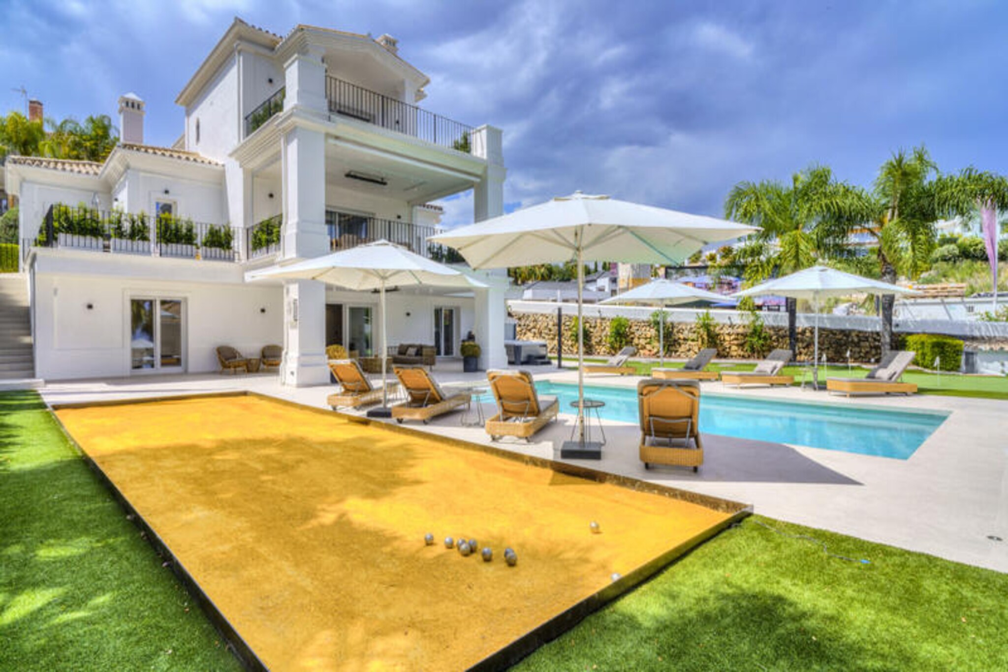In the heart of the prestigious Nueva Andalucía, this exquisite villa offers a luxurious retreat just minutes from the vibrant Puerto Banús. Surrounded by the lush greenery of world-class golf courses and the sparkling Mediterranean, this recently renovated property combines modern sophistication with timeless elegance. Whether you’re seeking relaxation or adventure, this villa is the perfect base for an unforgettable holiday on the Costa del Sol.
Step inside and discover a spacious haven designed for comfort and style. The villa features four double bedrooms and a family room with two single beds, accommodating up to twelve guests. The master suite boasts a walk-in closet, while all bedrooms offer ample wardrobe space. The open-plan living and dining area is bathed in natural light, leading to a fully equipped modern kitchen. Downstairs, a bar area opens onto the pool and games area, complete with a large jacuzzi, table tennis, and a pétanque court. Outside, the heated pool, putting green, and al fresco dining spaces invite you to unwind in the Mediterranean sunshine.
Situated just 400 meters from Los Naranjos Golf Club and 900 meters from La Quinta Golf Club, this villa is a golfer’s paradise. The beaches and marina of Puerto Banús are a mere two kilometers away, offering exclusive shopping, fine dining, and vibrant nightlife. Explore Marbella’s historic old town, with its charming cobbled streets, ancient Roman walls, and the iconic Orange Square. For day trips, the cultural treasures of Ronda, Granada, and Seville are within easy reach, as is the Sierra Nevada for a unique skiing experience.
Whether you’re savoring the local cuisine, practicing your golf swing, or simply soaking in the villa’s luxurious amenities, this property promises a holiday filled with relaxation, adventure, and unforgettable memories.