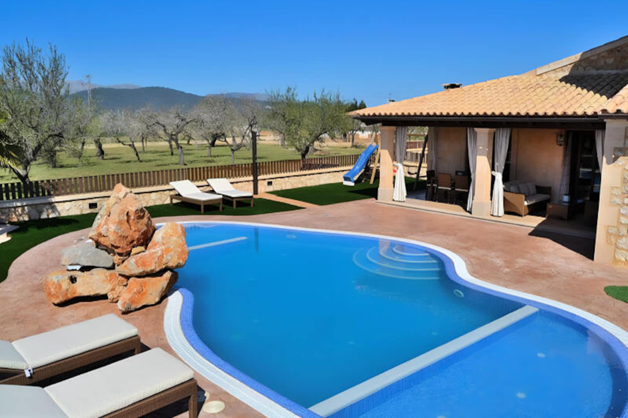 In the heart of Mallorca’s serene countryside, this stunning villa offers the perfect retreat for families and groups seeking both luxury and tranquility. Surrounded by the picturesque charm of Buger, a quaint Balearic village known for its cobbled streets and traditional stone houses, this property is a haven for relaxation and exploration. Whether you’re soaking up the Mediterranean sun or venturing out to discover the island’s hidden gems, this villa provides an idyllic base for your holiday. \n\nStep inside to discover a spacious and modern interior designed to accommodate up to eight guests. The villa features four comfortable bedrooms, including a master suite with an en-suite bathroom, and three additional bedrooms with twin beds. With three separate bathrooms, everyone can enjoy privacy and convenience. The bright and airy living room invites you to unwind on plush sofas, while the fully equipped kitchen, complete with top-of-the-line appliances, makes preparing meals a pleasure. \n\nOutside, the villa truly shines. A large garden surrounds a sparkling swimming pool, perfect for cooling off on warm summer days. Children will delight in the dedicated play area, while adults can relax on the sun loungers or enjoy al fresco dining in the peaceful outdoor space. The villa’s location ensures both privacy and easy access to Mallorca’s stunning beaches, just a 15-minute drive away. \n\nWith its blend of modern comfort, family-friendly amenities, and proximity to the authentic charm of Buger, this villa promises an unforgettable Mallorcan escape. Whether you’re seeking adventure or serenity, this is the perfect place to create lasting memories.
