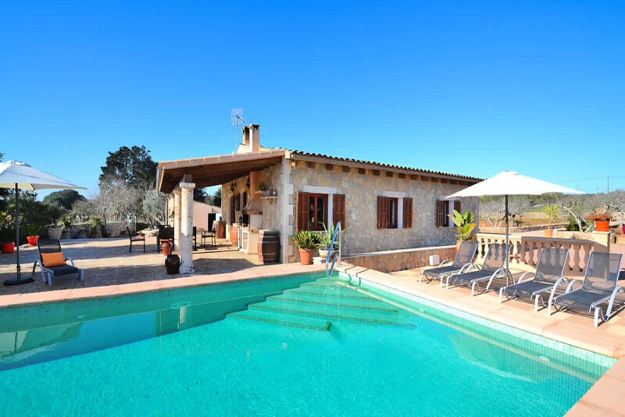In the heart of Mallorca’s serene countryside, this charming stone house offers a tranquil retreat just 1 km from the picturesque village of Ariany. Surrounded by golden fields and rolling hills, this property invites you to experience the authentic beauty of rural Mallorca, far from the hustle and bustle of mass tourism. Here, you’ll find the peace and relaxation you’ve been longing for, with the island’s natural charm as your backdrop. \n\nThe house spans 120 square meters, featuring three tastefully decorated bedrooms—one with a double bed and two with twin beds—making it ideal for families or small groups. Two modern bathrooms with showers ensure comfort for all guests. The spacious kitchen, equipped with all modern conveniences, is perfect for preparing meals to enjoy in the cozy dining area or outdoors. The bright and welcoming living room, complete with satellite TV, WiFi, and a fireplace, provides a perfect space to unwind after a day of exploration. \n\nStep outside to discover a beautifully maintained outdoor area that’s nothing short of spectacular. The large swimming pool (9x4m) is surrounded by a sun-drenched terrace with comfortable loungers, while the shaded lounge areas and barbecue space invite you to savor long, leisurely evenings under the stars. For added fun, a ping-pong table is also available. \n\nAriany’s charm lies in its peaceful streets and authentic Mallorcan culture. The surrounding area offers opportunities for scenic walks, cycling, and exploring nearby historical sites. Whether you’re seeking a serene escape or a base to discover Mallorca’s treasures, this stone house is the perfect choice for an unforgettable holiday.