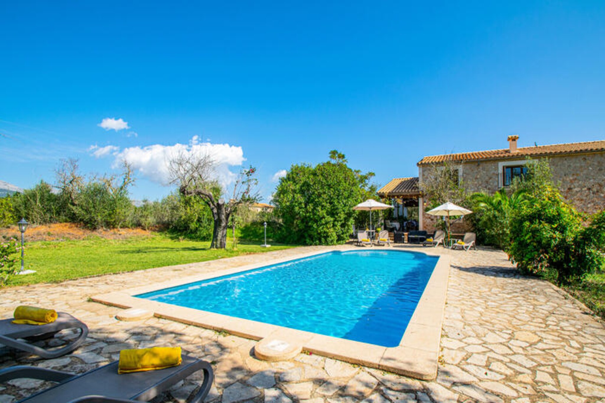 Amidst the rolling hills of the Majorcan countryside, this stunning country house near Buger offers a tranquil retreat for those seeking peace and comfort. Surrounded by lush Mediterranean landscapes, this spacious property spans 250 square meters and accommodates up to 11 guests, making it ideal for families or groups of friends. Here, the charm of rural Mallorca blends seamlessly with modern amenities, creating a haven of relaxation and connection. \n\nThe ground floor boasts three beautifully decorated bedrooms, two bathrooms (one with a shower and the other with a bathtub), a fully equipped kitchen, and a cozy living-dining area perfect for gathering together. Upstairs, the first floor features two additional bedrooms, a second lounge area, and a full bathroom with both a bathtub and shower, ensuring privacy and convenience for all. Every corner of this home is designed with care, offering comfort and style in equal measure. \n\nStep outside into the expansive garden, where Mediterranean plants and trees create a serene oasis. The terrace invites you to enjoy al fresco dining under the stars, complete with a barbecue for memorable evenings. A private swimming pool provides a refreshing escape during warm summer days, while air-conditioned bedrooms ensure comfort year-round. Whether you’re lounging by the pool or sharing meals on the terrace, every moment here feels special. \n\nLocated just 500 meters from Buger, this property is perfectly situated for exploring the charm of rural Mallorca. Buger’s cobbled streets and traditional stone houses exude authenticity, while its central location makes it an excellent base for discovering the island’s treasures. From nearby beaches to cultural landmarks, this home offers the perfect balance of seclusion and accessibility. Experience the magic of Mallorca in this unforgettable countryside retreat.