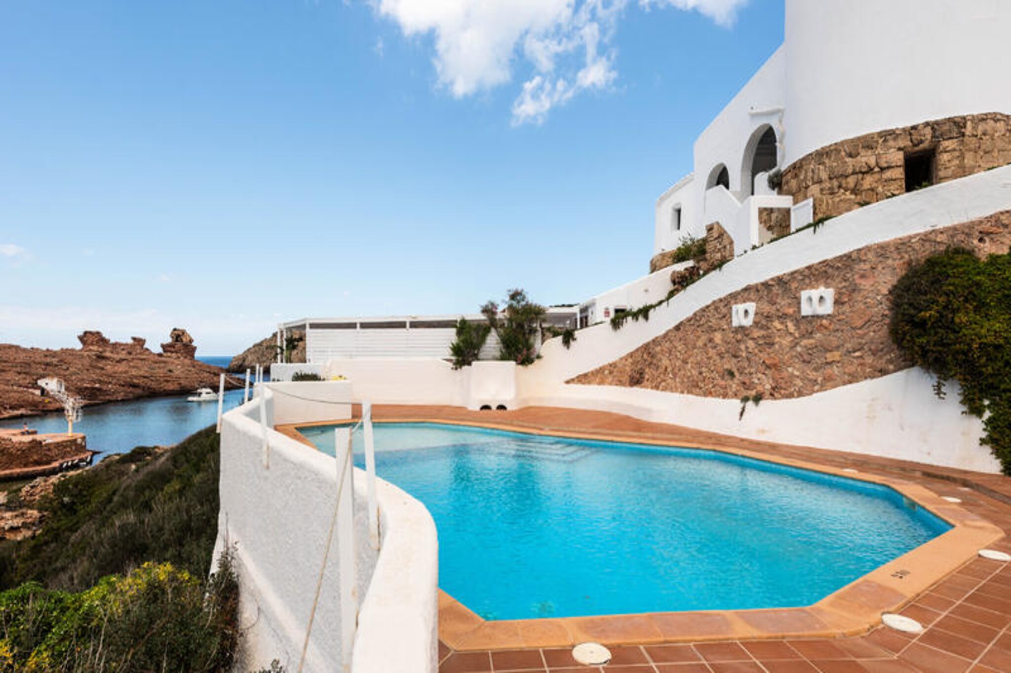 Where turquoise waters meet rugged cliffs, this charming apartment in Cala Morell offers a serene escape for families and couples alike. Imagine waking up to the gentle sound of waves and stepping onto your private terrace to soak in breathtaking views of the Mediterranean Sea and surrounding mountains. Just steps away from the sandy and rocky beaches of Cala Morell, this property invites you to immerse yourself in the natural beauty of Menorca’s coastline. Whether you’re seeking relaxation or adventure, this idyllic location delivers both in abundance. \n\nInside, the apartment is thoughtfully designed to combine comfort and practicality. With two cozy bedrooms, it comfortably accommodates up to four guests. The fully equipped kitchen, featuring an induction stove, refrigerator, microwave, and coffee maker, makes preparing meals a breeze. Modern amenities such as Wi-Fi, a television, and a washing machine ensure a seamless stay, while the communal swimming pool and on-site parking add convenience to your holiday experience. The 10 m² terrace is perfect for unwinding with a glass of local wine as the sun sets over the horizon.\n\nBeyond the property, Cala Morell offers a wealth of attractions to explore. The vibrant city of Ciutadella is just 7 km away, where you can wander through historic streets, sample Menorcan cuisine, or shop for unique souvenirs. Golf enthusiasts will appreciate the proximity to Club Son Parc, while nature lovers can venture to nearby trails and coves for unforgettable hikes. With Menorca Airport only 40 km away, your journey to tranquility is effortless.\n\nWhether you’re drawn by the promise of sun-soaked days on the beach, cultural excursions, or simply a peaceful retreat by the sea, this apartment is your gateway to the magic of Menorca. Let the charm of Cala Morell captivate you and create memories that will last a lifetime.
