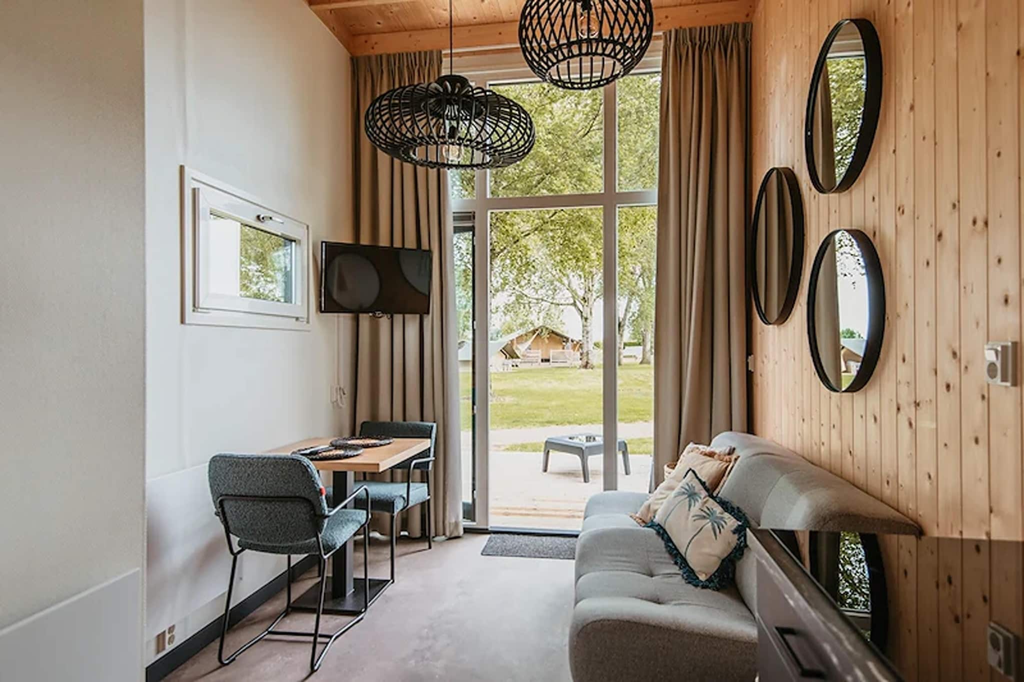 There’s a moment, just after you arrive at Tiny Lodge, when everything fades into slow - the water settles into a soft shimmer, the trees sway lightly overhead, and you realize this is exactly the quiet you’ve been craving together. Placed inside De Betuwse Hofjes, your glamping lodge becomes a private cocoon for two: warm, calming and wrapped in nature’s stillness.

Inside, the wooden exterior shell opens into a surprisingly elegant space. A snug living area invites with a dining table and a sofa for 2, and the well-equipped kitchen lets you prepare breakfast side by side. Step out of the house, and it becomes your very own garden where you can savour your morning coffee with lake reflections at your feet and end the day with wine as the sky melts into dusk. The double bedroom is neatly tucked on the mezzanine in the house, with a low ceiling for convenience. For added comfort, you get Wi-Fi, electricity and free parking.

Spend your days however you please. Swim hand-in-hand in the clear lake, wander barefoot along the sandy shore, or stretch out on the grass together with nothing but time to fill. Explore nearby orchards and quiet countryside lanes, stop at a village café, or rent bikes for an afternoon adventure through the Betuwe’s scenic roads.

Return to your lodge as night settles - cook a simple dinner – enjoying it indoors or outdoors up to you, listen to the soft ripple of the lake and feel the world shrink to just the two of you. Betuwe Lodge isn’t just a getaway; it’s a gentle pause, a place where love meets peace, and where every moment feels warmly, beautifully unhurried.