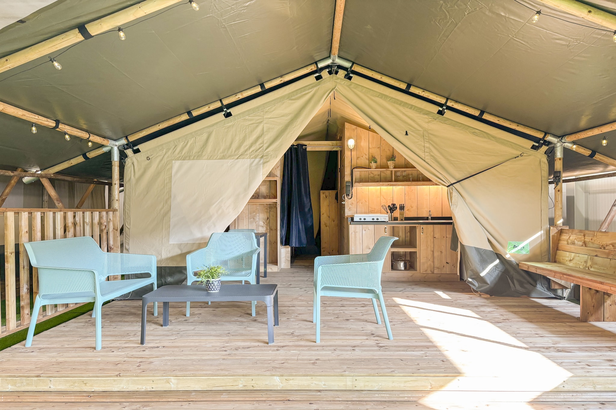 Imagine waking up to the gentle ripple of water and sunlight filtering through the canvas of your tent; that’s how a day begins at a Blossom Camp placed inside De Betuwse Hofjes. This peaceful retreat blends the charm of the wild with the comfort of a fully equipped home if it were without walls, making it ideal for those wanting to connect with nature.

Inside the tent, you will only have a simple sleeping arrangement with two bedrooms furnished with a double bed or two single beds and two bunk bed, respectively, easily housing 6 people for the night, and a private bathroom with essentials, rest all the other areas of the house count as outdoors, consisting of an actual bright living area, a dining space all flowing into the veranda, and an open kitchen with essential needed for cooking You get access to Wi-Fi and electricity.

Around you, the estate feels like a living postcard. A swimming lake with a sandy shore, calm fishing spots, green paths, and small play areas brings a sense of freedom to your stay. Whether you swim, wander barefoot along the edge, try the air-trampoline or simply soak in the quiet, every moment feels refreshingly uncomplicated.

Hop on a bike to explore the region, gliding through orchards, riverbanks, village cafés and the wide, open Dutch countryside. With free parking and Wi-Fi, you can plan as much or as little as you want.

Nights here are easy as you savour shared dinners outdoors, long conversations under the moonlit sky, and the kind of rest that only nature can offer.