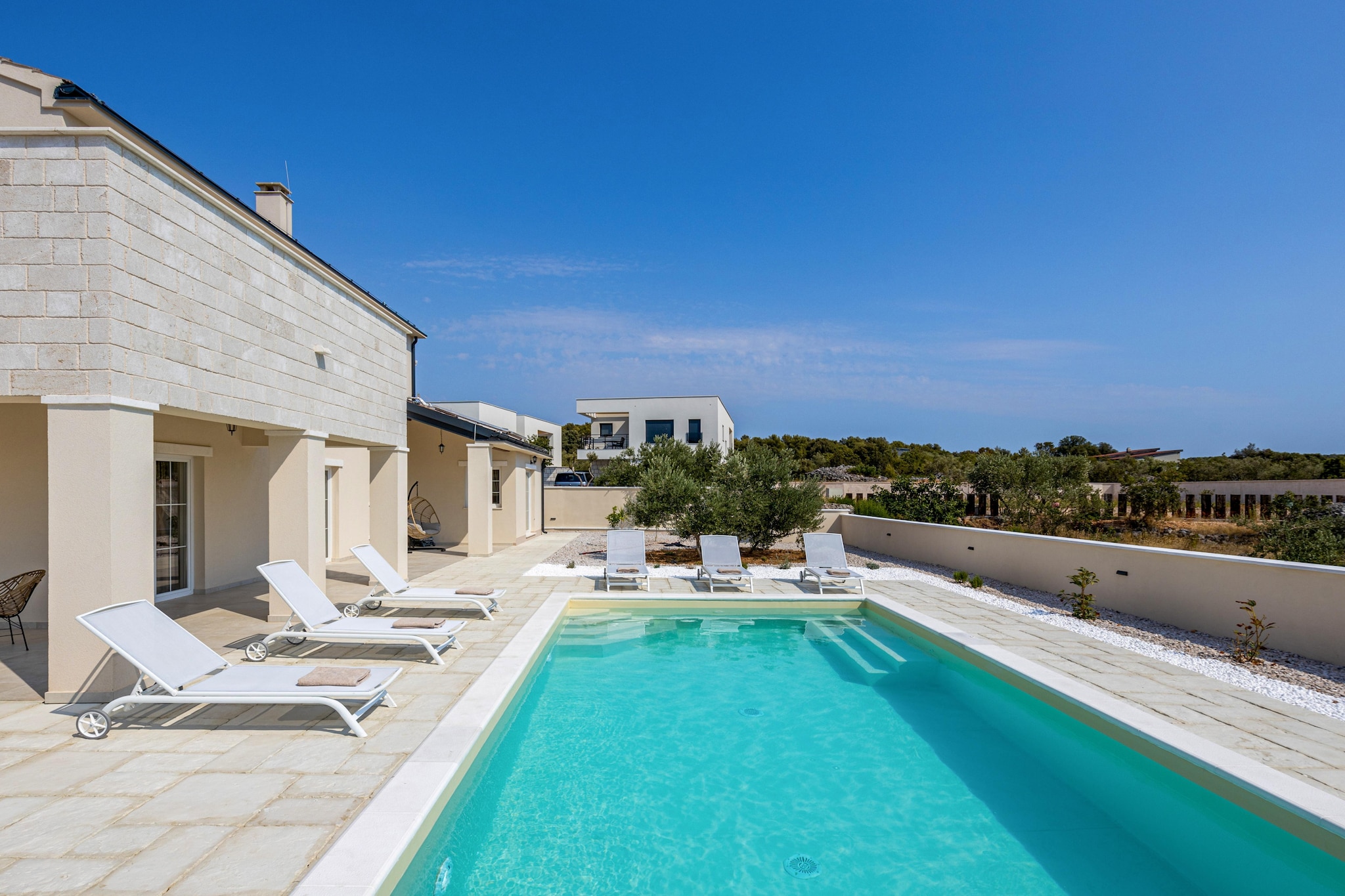 Just a short walk from the shoreline in the laid-back town of Jezera, Villa Royal Stone brings together modern comfort and relaxed Mediterranean living. Built on a generous 990 m² plot, this spacious villa is designed for families or groups of friends who want privacy, space and easy access to the sea.
The living space unfolds with a warm, contemporary feel. The living-dining room is inviting and social, with a comfortable convertible sofa, fireplace, a dining table and TV, flowing into a fully equipped modern kitchen for effortless shared meals. The villa hosts three spacious bedrooms - two with double beds and one with twin beds that can be joined, and each bedroom includes its own en-suite bathroom supplied with essentials, offering comfort and independence for all guests.
Outdoor living is a true highlight. The terrace centres around a pool, surrounded by sun loungers, a covered dining area and a wood barbecue for long alfresco evenings. An upper-floor balcony with sea views offers a quieter corner for morning coffee or a late book. Guests also have access to a private gym, children’s outdoor play equipment and bicycles for local exploring.
The villa is just 350 metres from the beach, with restaurants, cafés and daily essentials within easy walking distance. Šibenik, Krka National Park and the wider Murter coastline add variety to day trips.
This home is best suited to travellers seeking a walk-to-the-beach location with full privacy, modern amenities and space to unwind together - without relying on a car for every outing. The balance of comfort, location and outdoor living makes it a practical yet indulgent coastal base.