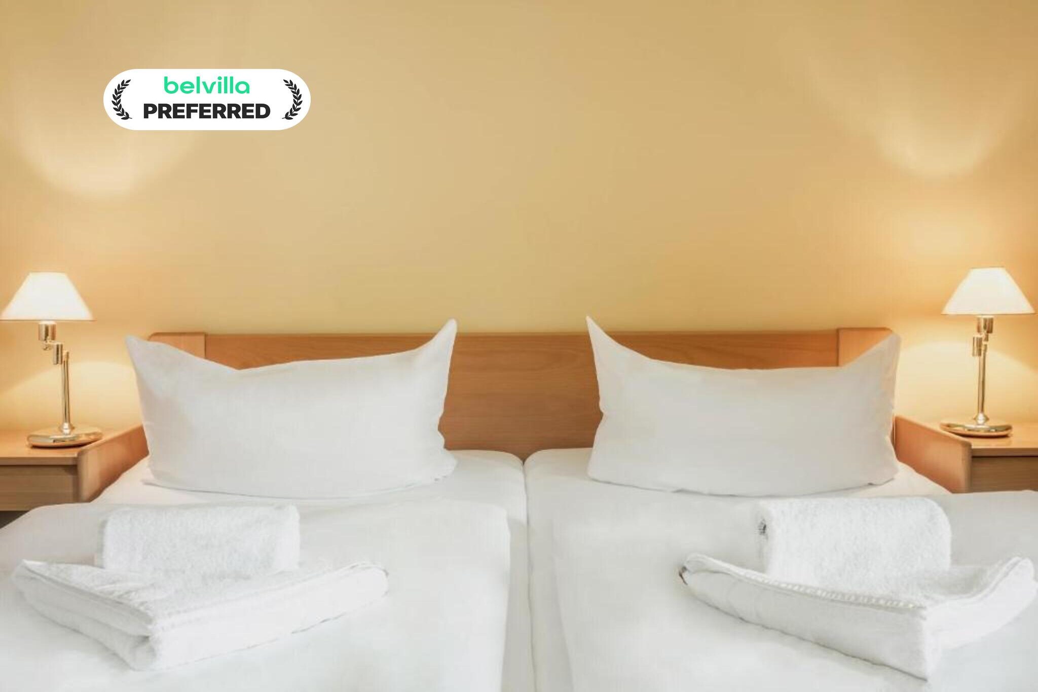 Situated in the peaceful Feldberg Lake District, this Standard Suite Room at Kaiserhof Feldberg by Belvilla Resorts offers a spacious and comfortable base for families or small groups. Surrounded by lakes, forests, and fresh countryside air, the hotel lies in the heart of the state-approved Kneipp spa town of Feldberg, close to walking paths, spa trails, and nature-filled scenery ideal for a relaxed yet refreshing stay.
Standard Suite Room Features
1. Spacious suite with a separate living room and bedroom
2. Two extra-large double beds plus one sofa bed
3. Two private bathrooms with bathtub and shower, towels, bathrobes, slippers, and toiletries
4. Flat-screen TV with cable, satellite channels, and streaming services like Netflix
5. Free Wi-Fi, minibar, refrigerator, and safety deposit box
6. Seating area, desk, soundproof walls, and hypoallergenic finishes
7. Garden and city views with plenty of natural light
8. Non-smoking suite with generous wardrobe space
9. Pet-friendly (additional charge of 12 Euro/pet/night)
Hotel Amenities & Guest Perks
1. Games and leisure options including billiards, darts, archery, mini golf, water sports, cycling, hiking, horse riding, fishing, and evening entertainment
2. Garden, terrace areas, and sun loungers
3. On-site restaurant and bar
4. Lift access throughout the hotel
5. Paid parking Euros 5 per vehicle per day
6. Reception available from 6:00 to 11:00 in the morning and from 15:00 to 18:00 in the afternoon
Nearby Attractions
1. Feldberg Lake and town church – walking distance
2. Kneipp Spa Park – approx. 150 m
3. Forest trails and cycling routes nearby
4. Schloss Tornow – approx. 47 km
How to Reach
1. By train: Neustrelitz or Neubrandenburg stations, then bus or taxi
2. By air: Heringsdorf Airport – approx. 117 km